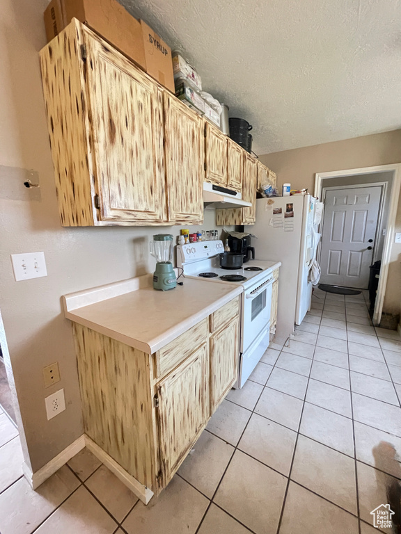 Kitchen with white appliances, under cabinet range hood, a textured ceiling, light countertops, and light tile patterned floors