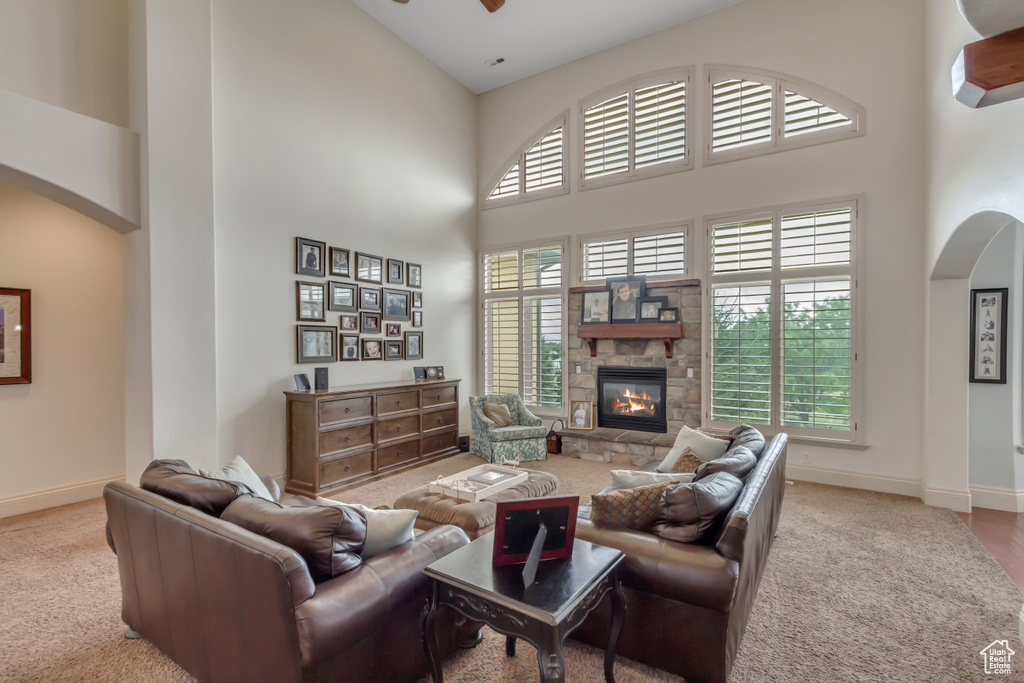 Carpeted living room featuring a high ceiling, arched walkways, baseboards, a ceiling fan, and a fireplace