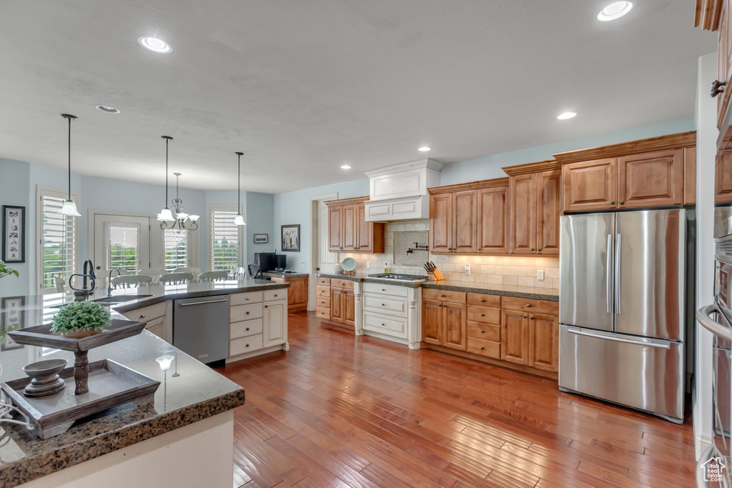 Kitchen with appliances with stainless steel finishes, decorative backsplash, light wood-style flooring, recessed lighting, and hanging light fixtures