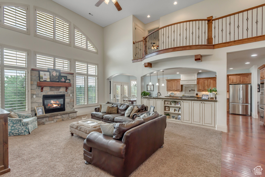 Living area featuring a towering ceiling, recessed lighting, a stone fireplace, ceiling fan, and light wood-style floors