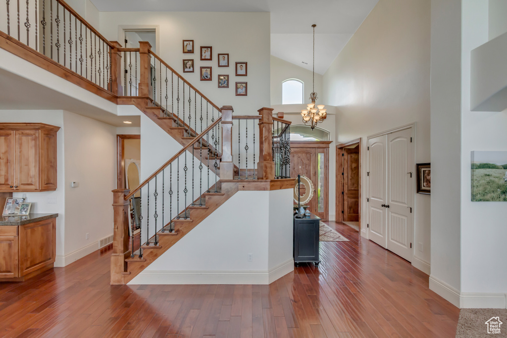 Staircase with high vaulted ceiling, hardwood / wood-style flooring, a chandelier, and baseboards