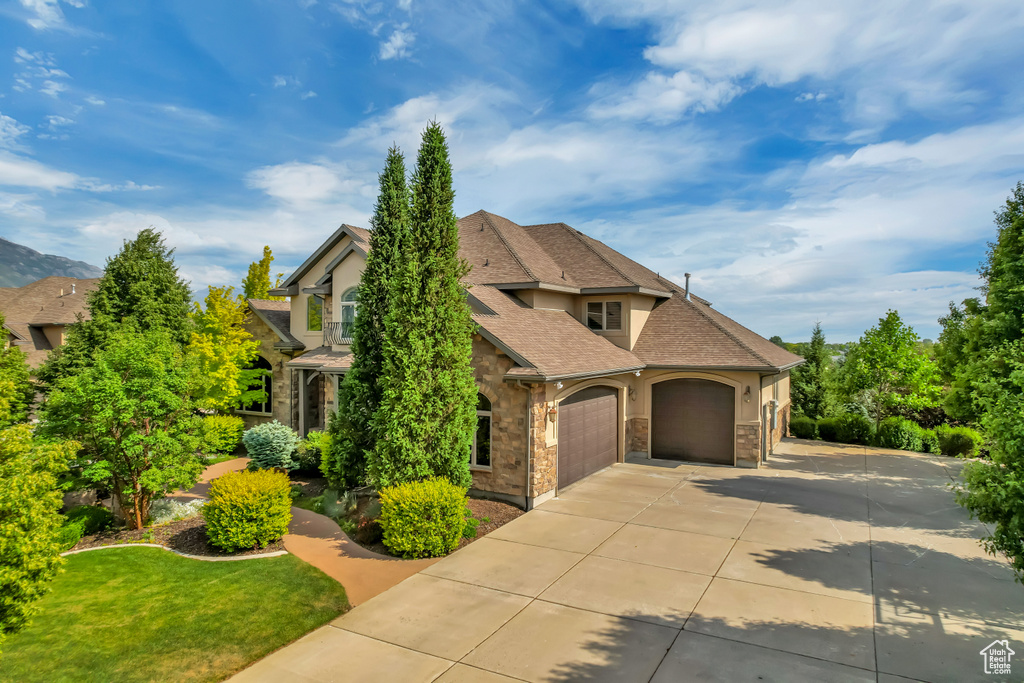 View of front of home featuring stone siding, a garage, concrete driveway, stucco siding, and a front lawn