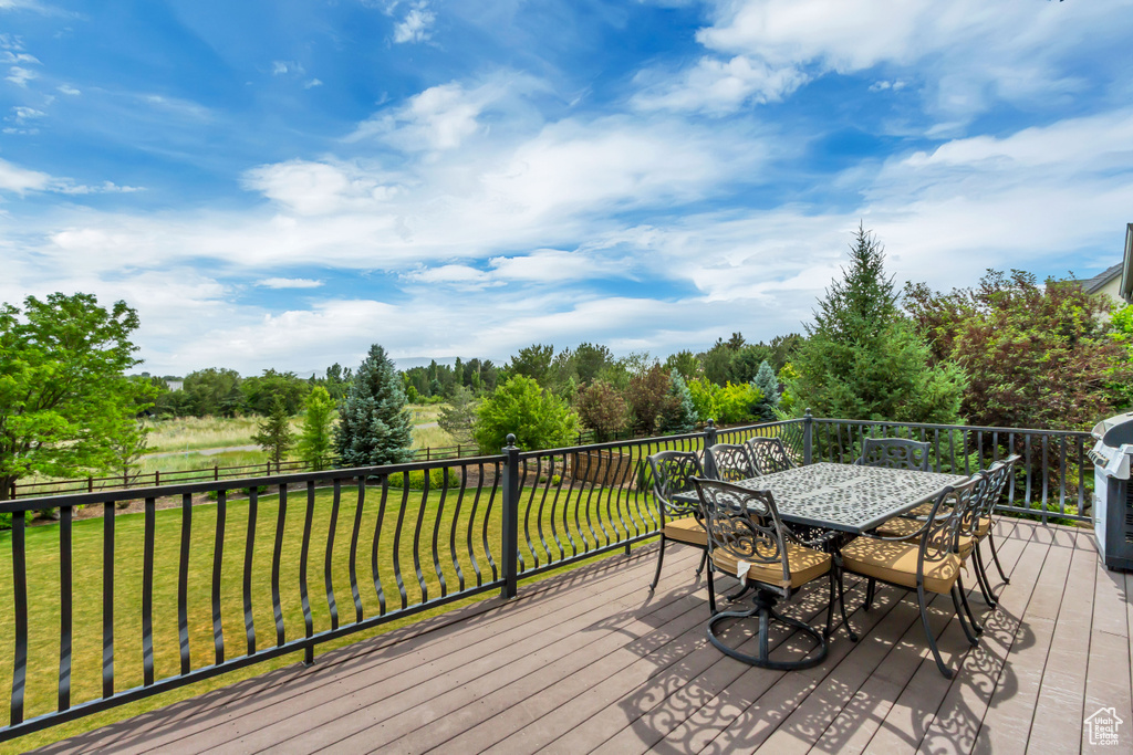 Wooden terrace with outdoor dining space, a lawn, and view of scattered trees