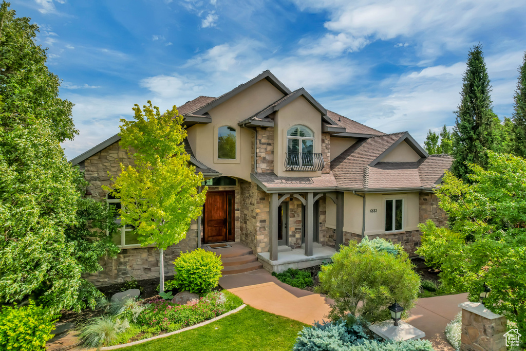 View of front of property with stone siding, stucco siding, a balcony, a porch, and a shingled roof