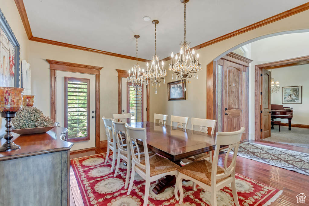 Dining area featuring arched walkways, baseboards, light wood-style floors, a chandelier, and ornamental molding