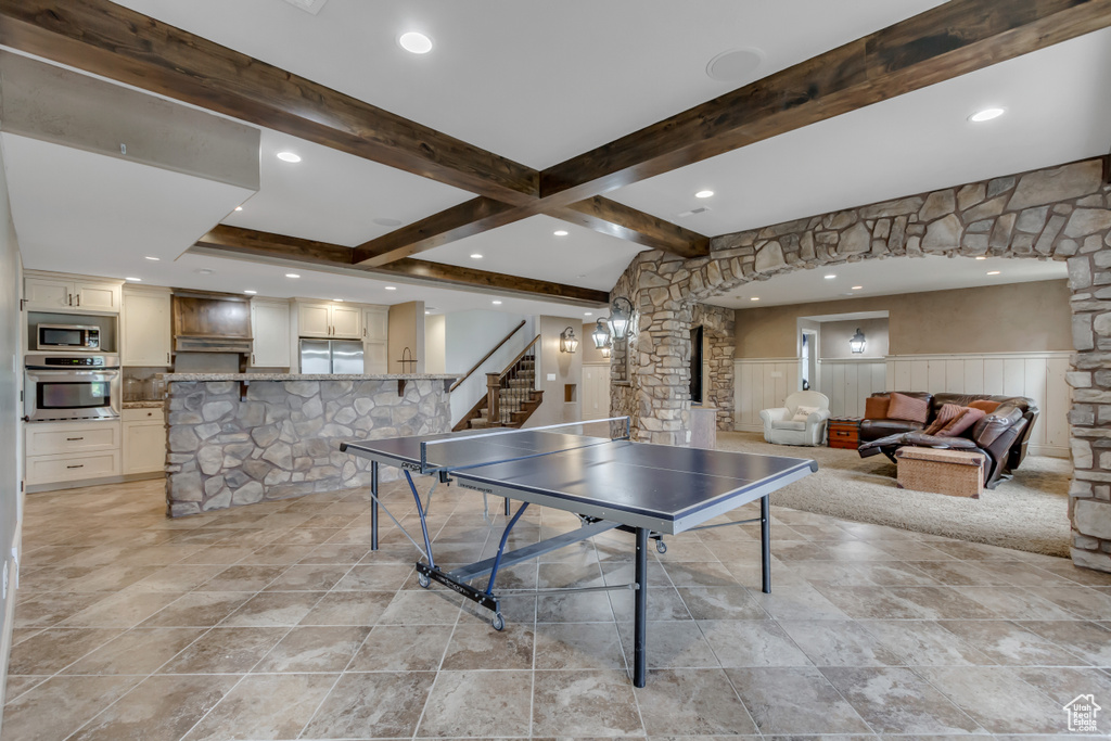 Recreation room featuring beam ceiling, wainscoting, decorative columns, recessed lighting, and light stone finish floors
