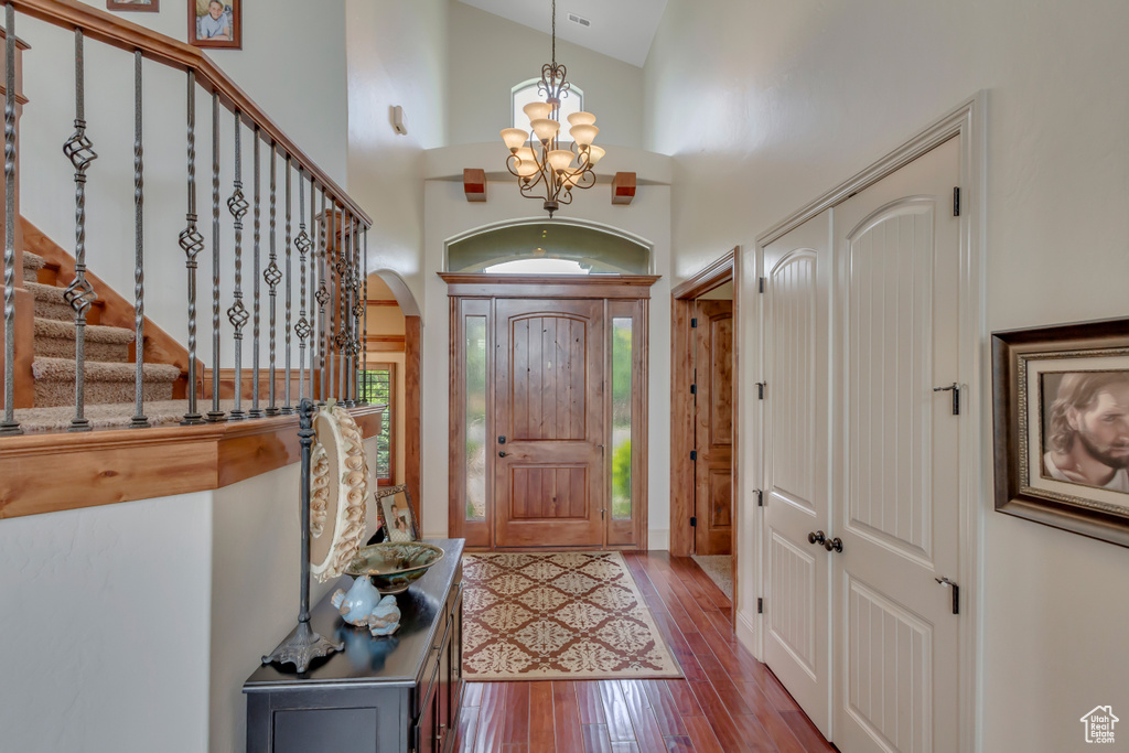 Entrance foyer featuring a chandelier, wood-type flooring, high vaulted ceiling, arched walkways, and stairs