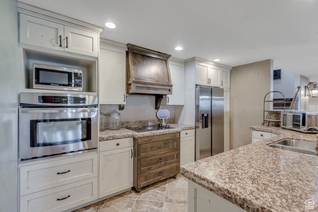 Kitchen with appliances with stainless steel finishes, custom range hood, a sink, light stone counters, and recessed lighting