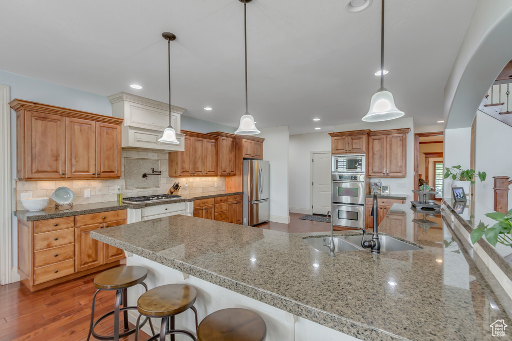 Kitchen featuring appliances with stainless steel finishes, a sink, a breakfast bar, backsplash, and light stone countertops