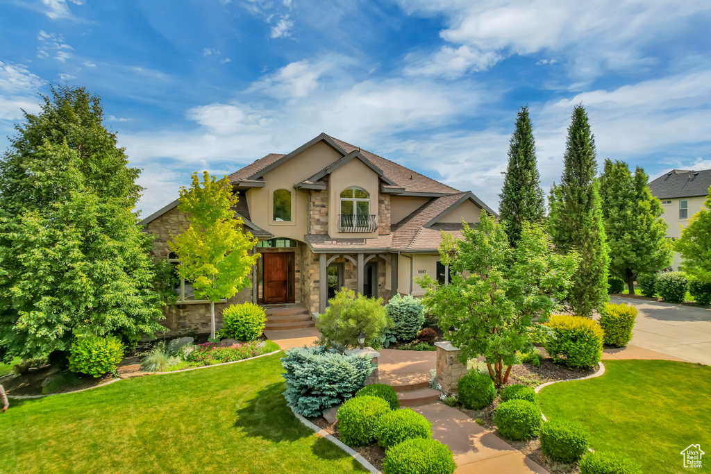 Traditional-style home with stucco siding, stone siding, a front yard, and a shingled roof