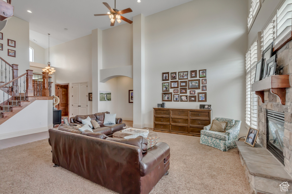 Carpeted living room with a stone fireplace, a towering ceiling, stairway, ceiling fan, and arched walkways