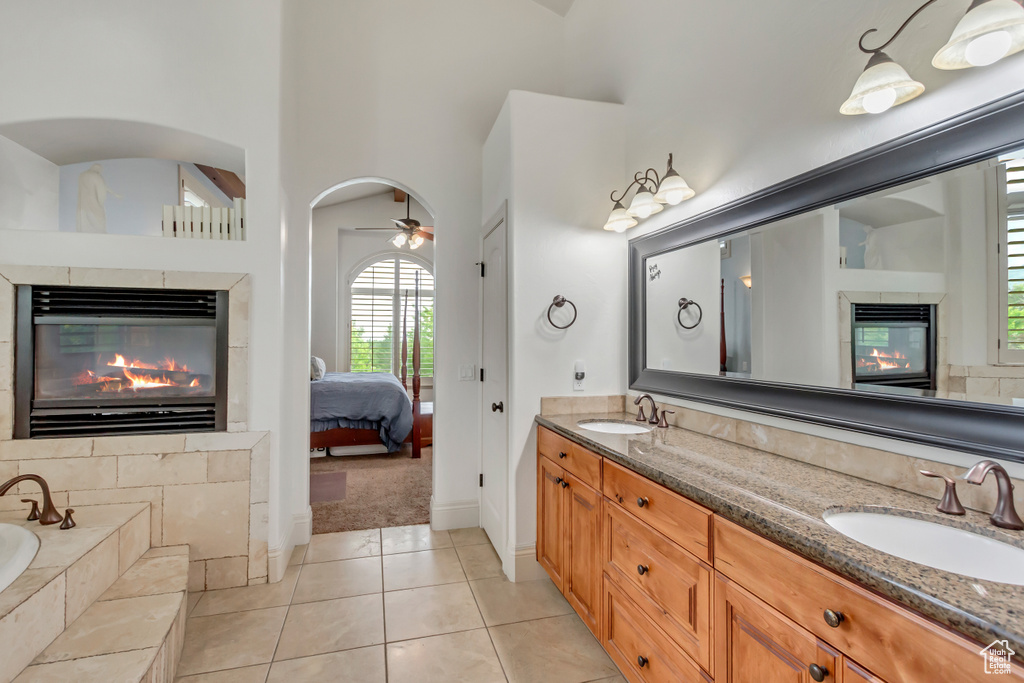 Ensuite bathroom featuring a multi sided fireplace, double vanity, a garden tub, tile patterned floors, and baseboards
