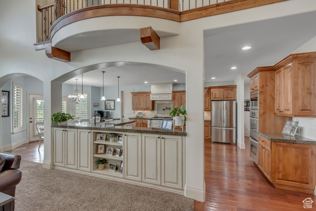 Kitchen with stainless steel appliances, arched walkways, a towering ceiling, dark stone counters, and recessed lighting