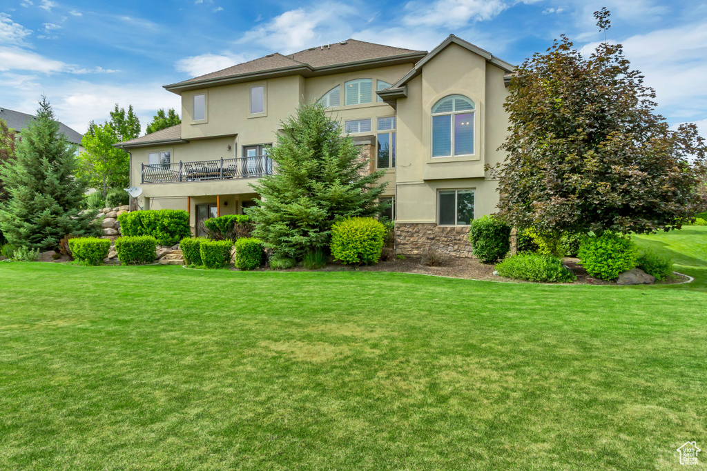 Rear view of house featuring stucco siding, a yard, a balcony, and stone siding