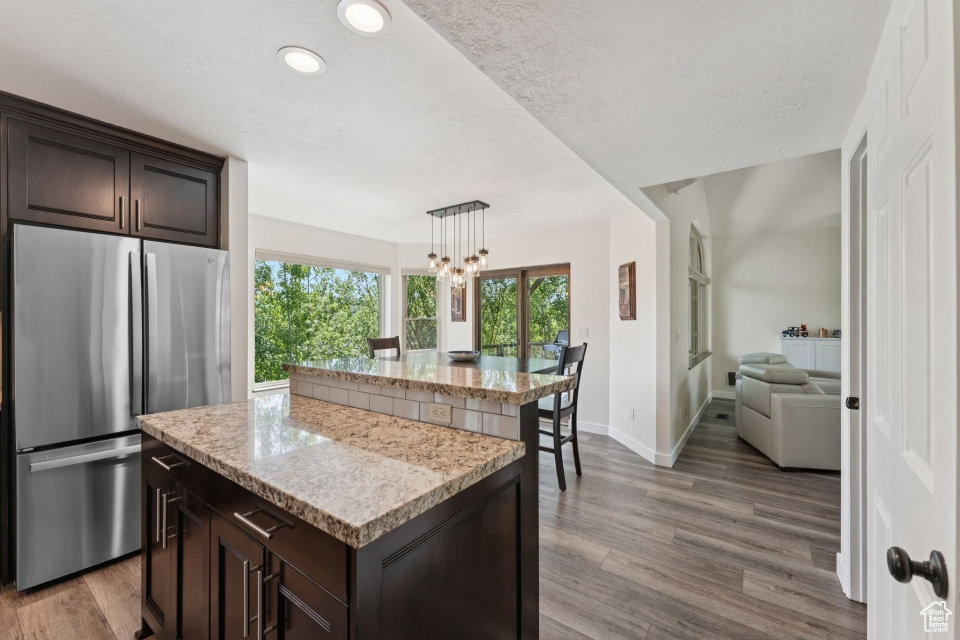 Kitchen featuring freestanding refrigerator, a center island, dark brown cabinetry, plenty of natural light, and a textured ceiling