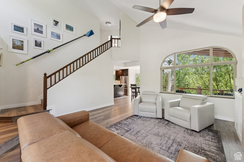 Living room with ceiling fan, wood finished floors, baseboards, high vaulted ceiling, and stairs