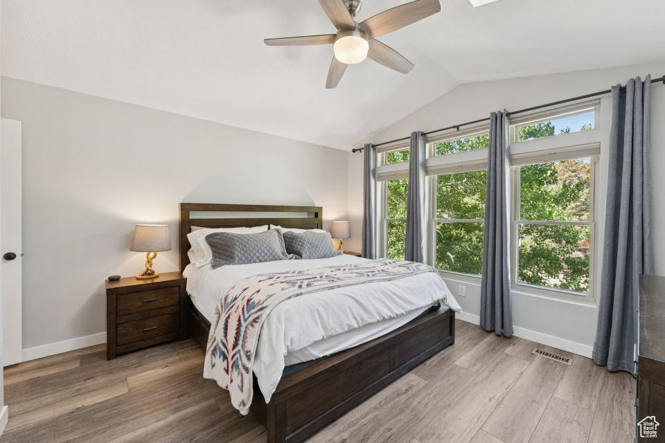 Bedroom featuring vaulted ceiling, multiple windows, baseboards, light wood-style floors, and a ceiling fan