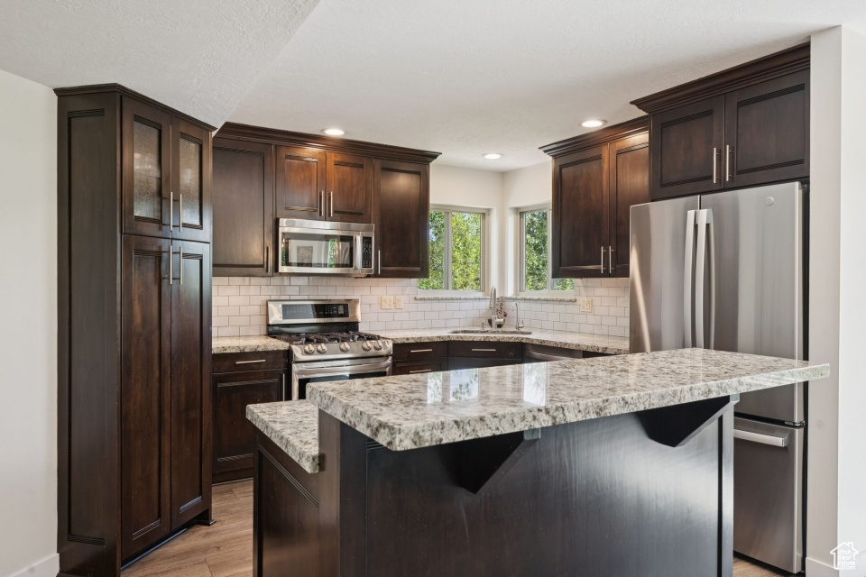 Kitchen featuring appliances with stainless steel finishes, a sink, light wood-style flooring, light countertops, and dark brown cabinetry