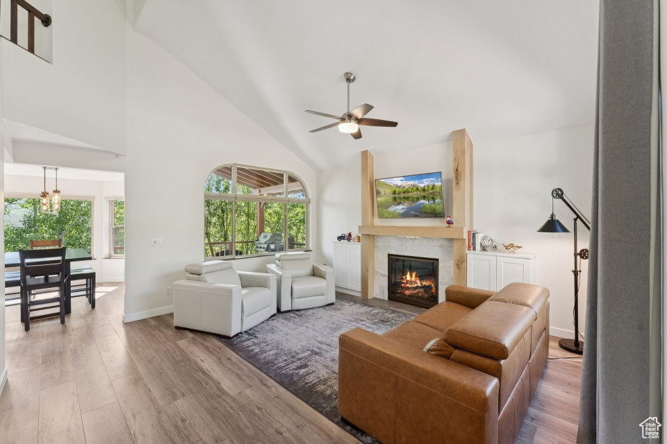 Living area with high vaulted ceiling, wood finished floors, a glass covered fireplace, a ceiling fan, and plenty of natural light