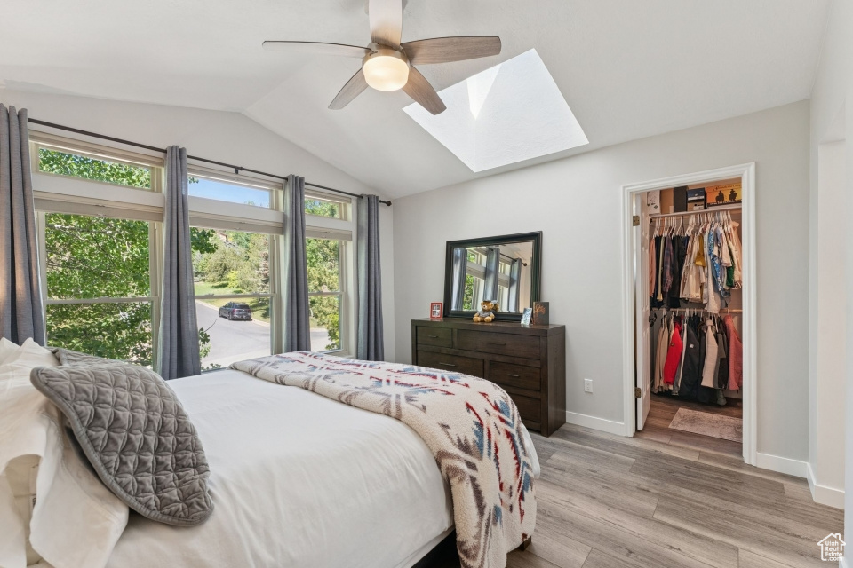 Bedroom with a skylight, lofted ceiling, light wood-style floors, a spacious closet, and baseboards