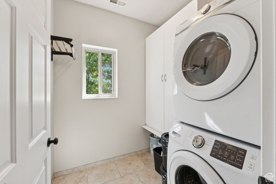 Laundry area with stacked washing machine and dryer, cabinet space, tile patterned flooring, and baseboards