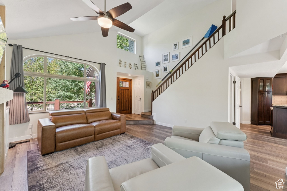 Living area featuring wood finished floors, a ceiling fan, high vaulted ceiling, baseboards, and stairway