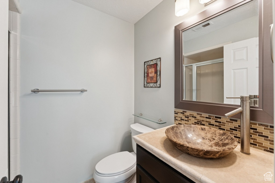 Bathroom featuring backsplash, vanity, toilet, and a shower with shower door