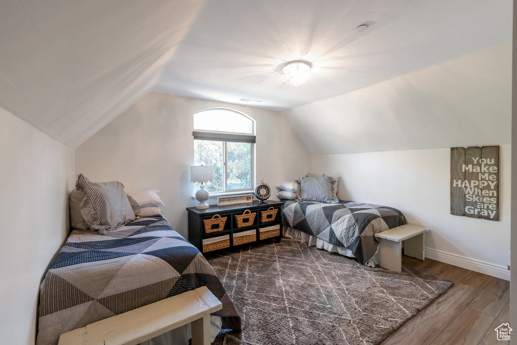 Bedroom with wood finished floors, lofted ceiling, and baseboards