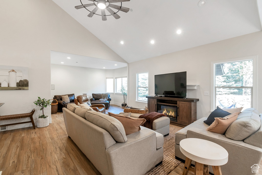 Living area with high vaulted ceiling, light wood-style floors, recessed lighting, a glass covered fireplace, and ceiling fan