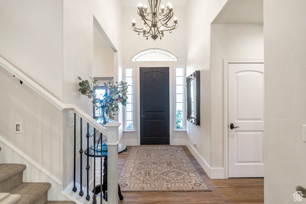 Entrance foyer with wood finished floors, a chandelier, a towering ceiling, stairs, and baseboards