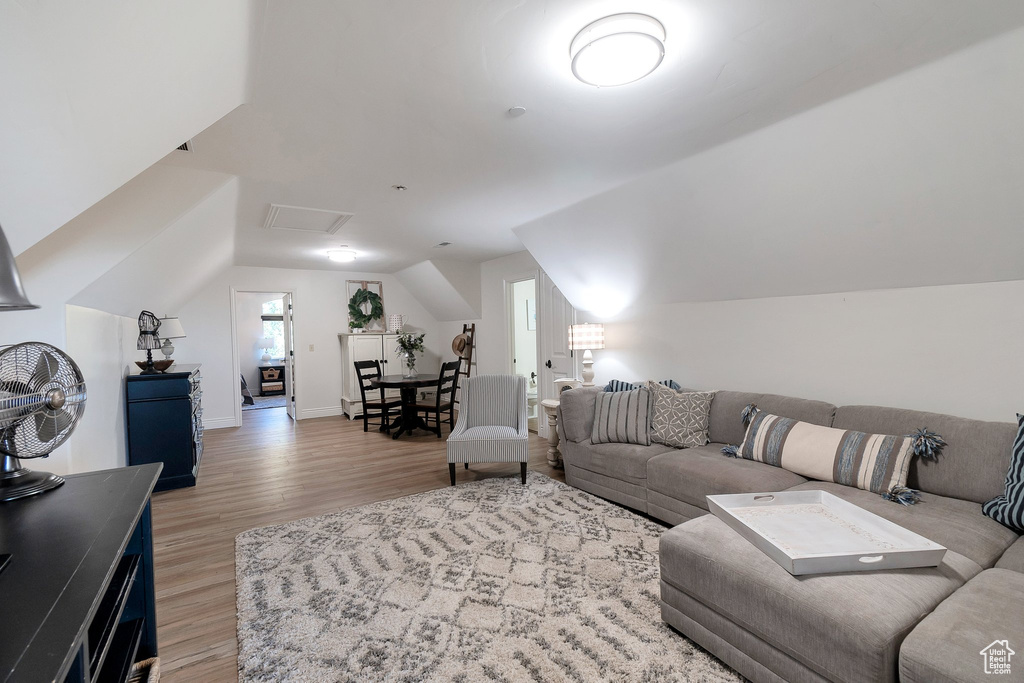 Living area with light wood finished floors, vaulted ceiling, baseboards, and attic access