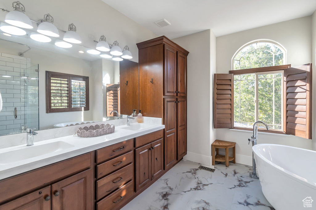 Bathroom featuring a soaking tub, double vanity, and healthy amount of natural light