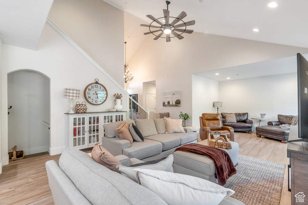 Living area featuring ceiling fan, stairway, light wood-style flooring, arched walkways, and high vaulted ceiling
