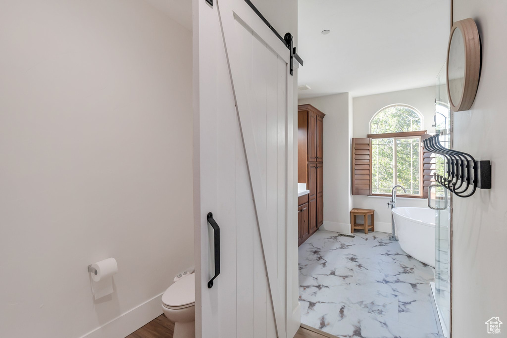 Full bath with toilet, a freestanding tub, vanity, marble finish flooring, and baseboards