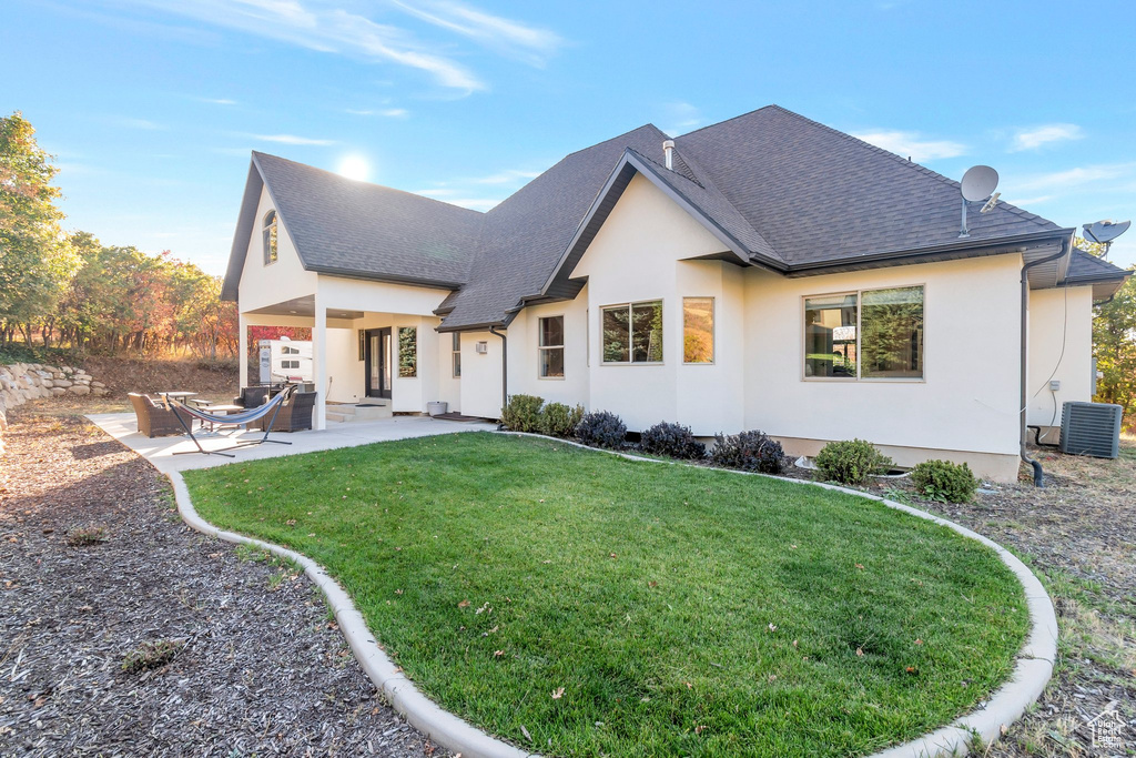 Back of house featuring central AC unit, roof with shingles, stucco siding, a yard, and a patio