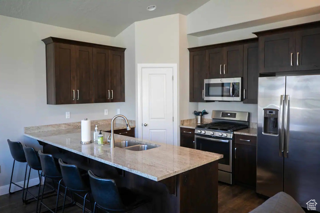 Kitchen featuring appliances with stainless steel finishes, a sink, dark wood-type flooring, and a breakfast bar area