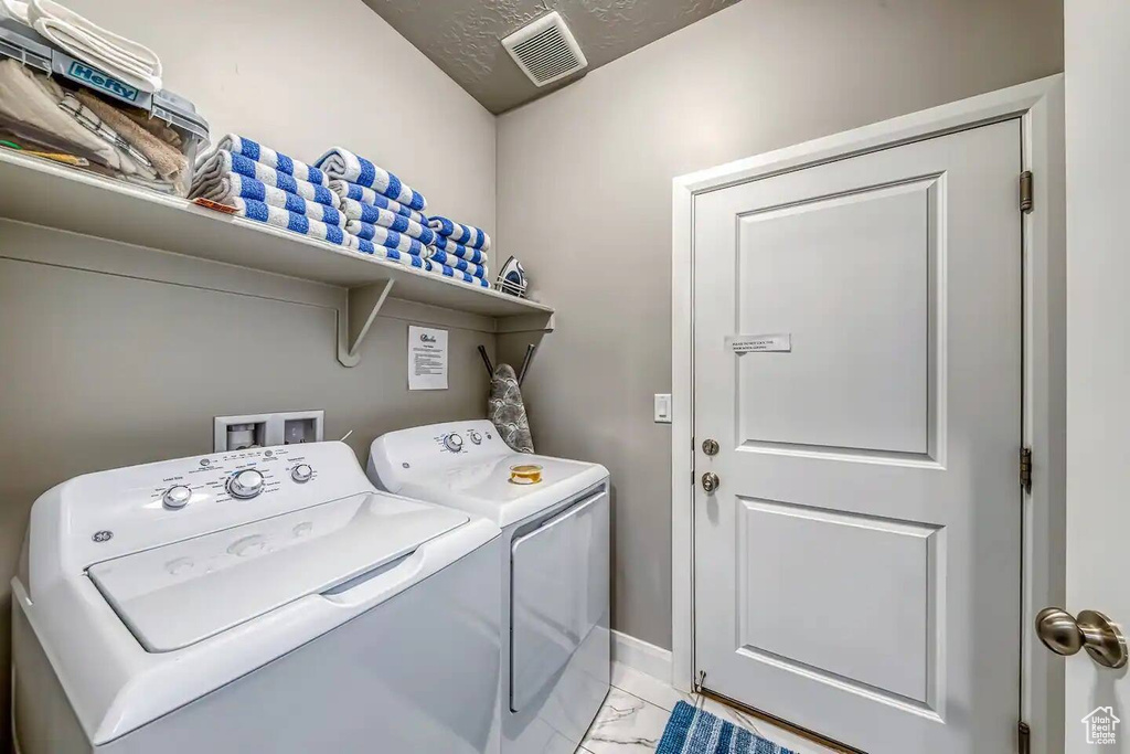 Laundry area featuring washing machine and clothes dryer, light marble finish flooring, and baseboards