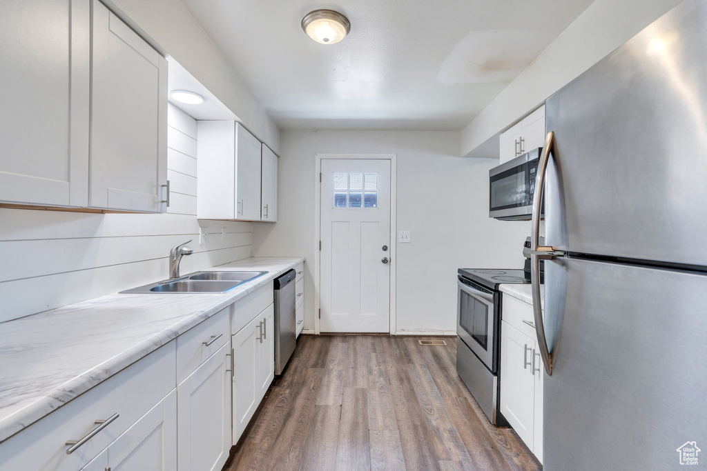 Kitchen featuring appliances with stainless steel finishes, a sink, white cabinetry, and wood finished floors