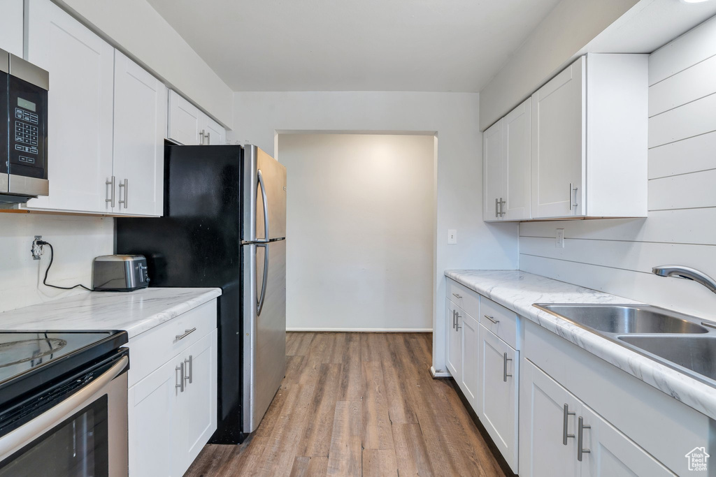 Kitchen with appliances with stainless steel finishes, white cabinets, light wood finished floors, a sink, and light stone countertops