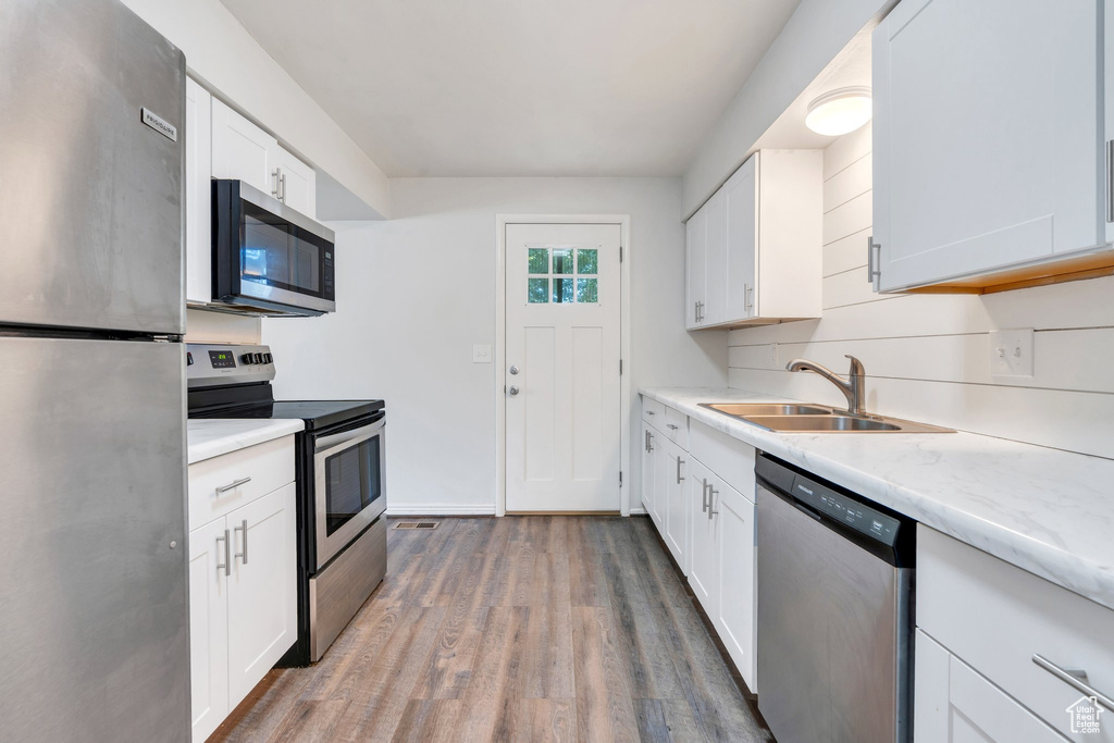 Kitchen featuring appliances with stainless steel finishes, wood finished floors, white cabinetry, and a sink