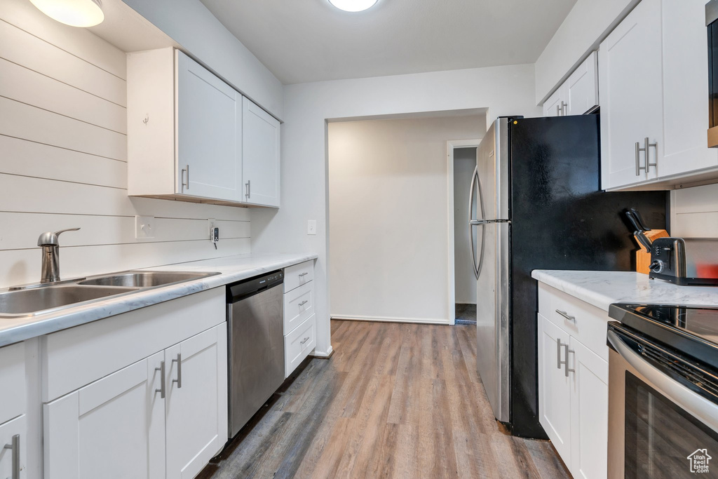 Kitchen featuring stainless steel appliances, a sink, light wood finished floors, light countertops, and white cabinetry