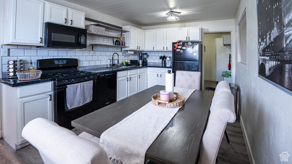 Kitchen featuring black appliances, dark countertops, decorative backsplash, a sink, and white cabinets