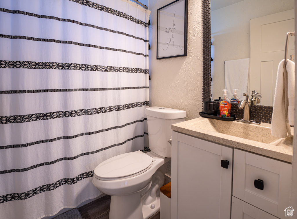 Bathroom with toilet, vanity, a textured wall, and curtained shower
