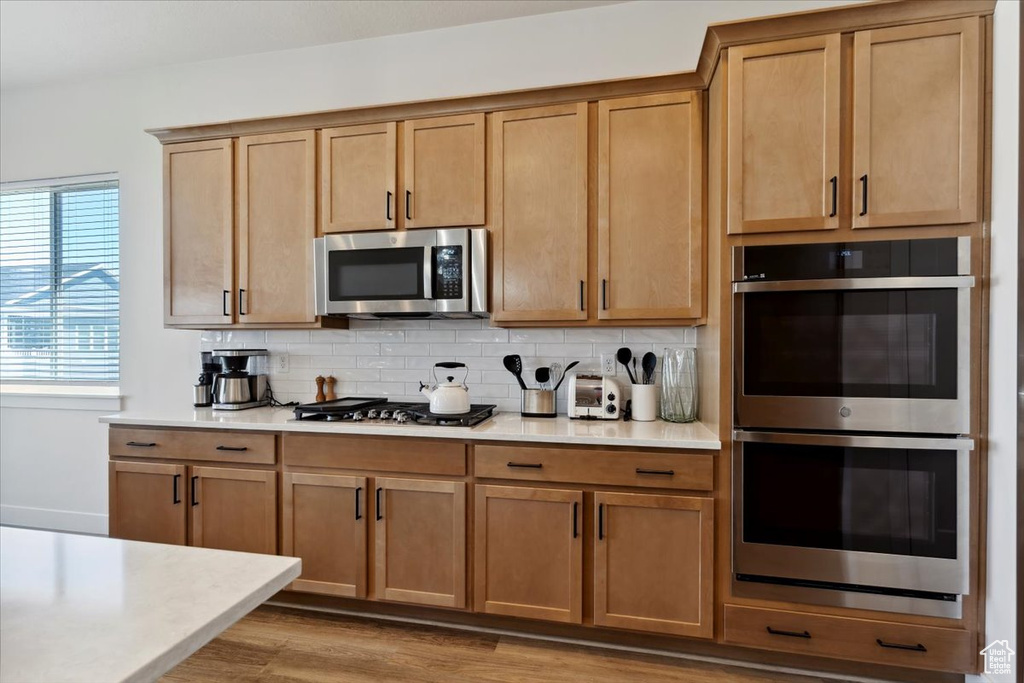 Kitchen with appliances with stainless steel finishes, decorative backsplash, light countertops, and light wood-style floors
