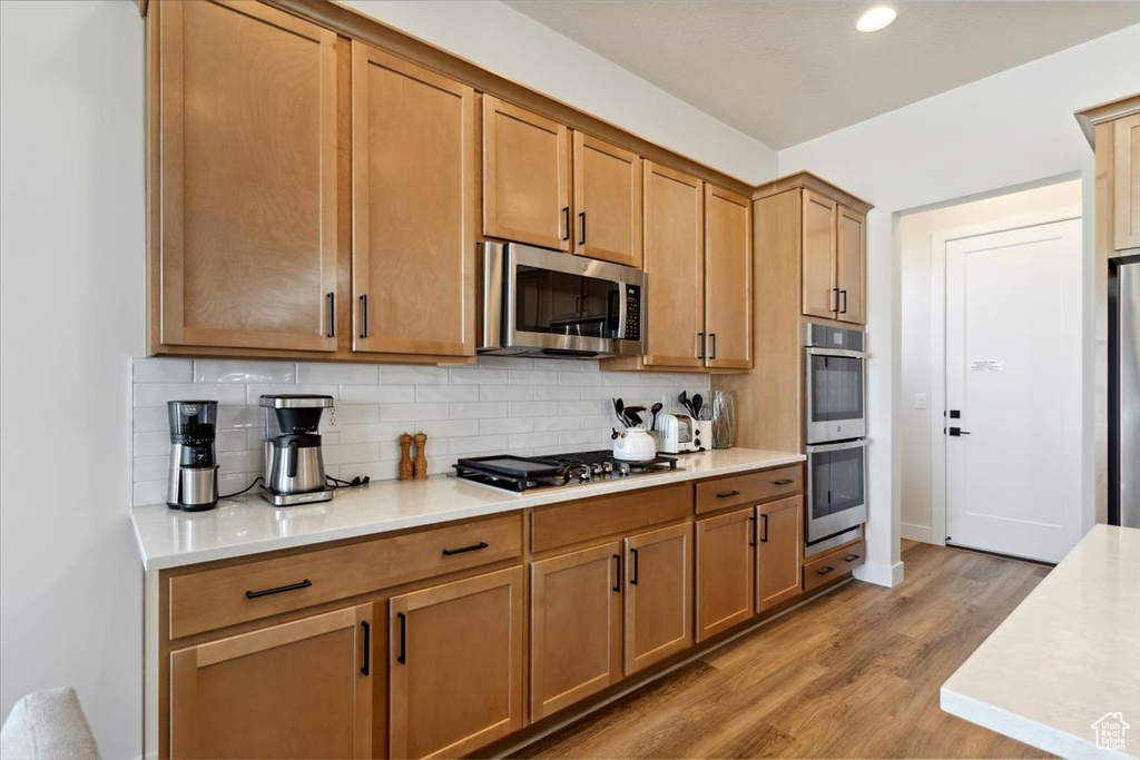 Kitchen with appliances with stainless steel finishes, light wood-style floors, backsplash, light countertops, and brown cabinetry