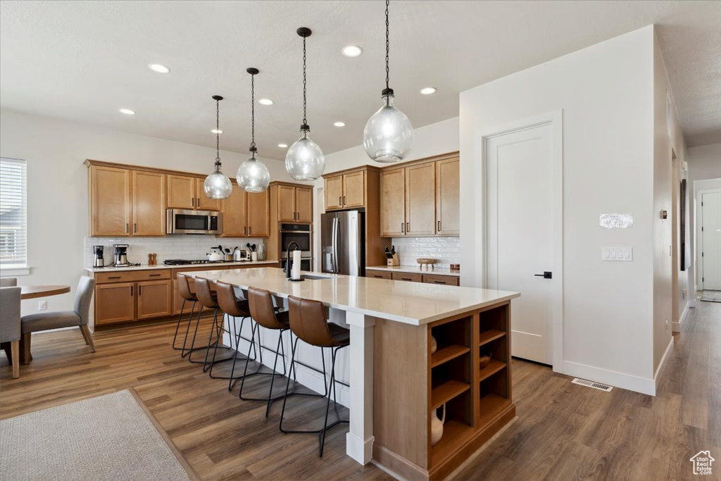 Kitchen featuring appliances with stainless steel finishes, recessed lighting, wood finished floors, and tasteful backsplash