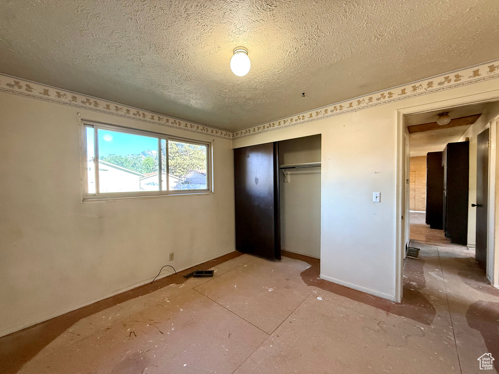 Unfurnished bedroom featuring a textured ceiling, baseboards, and a closet