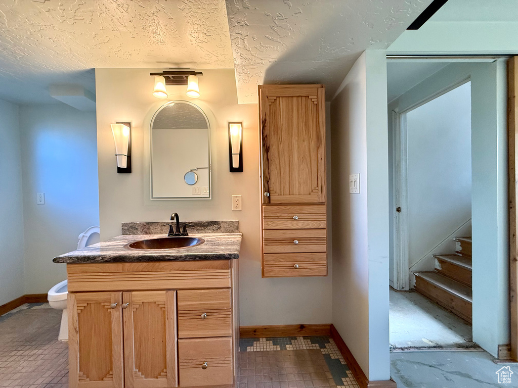 Bathroom with baseboards, vanity, toilet, and a textured ceiling