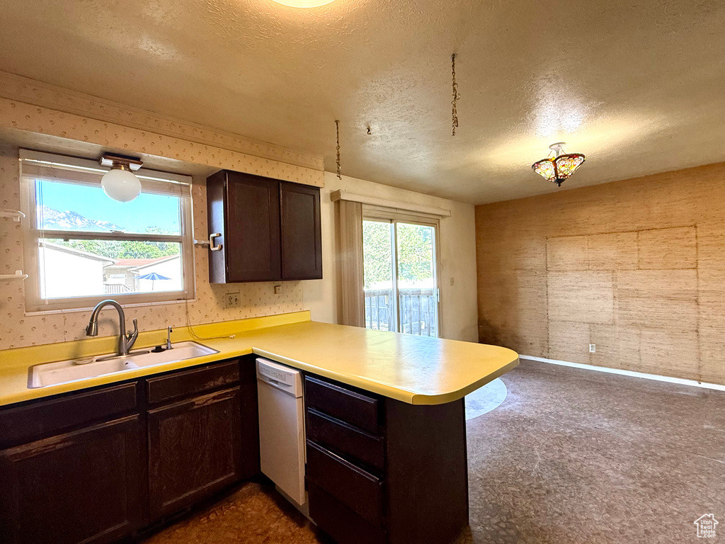Kitchen featuring dishwasher, wallpapered walls, a sink, a peninsula, and a textured ceiling