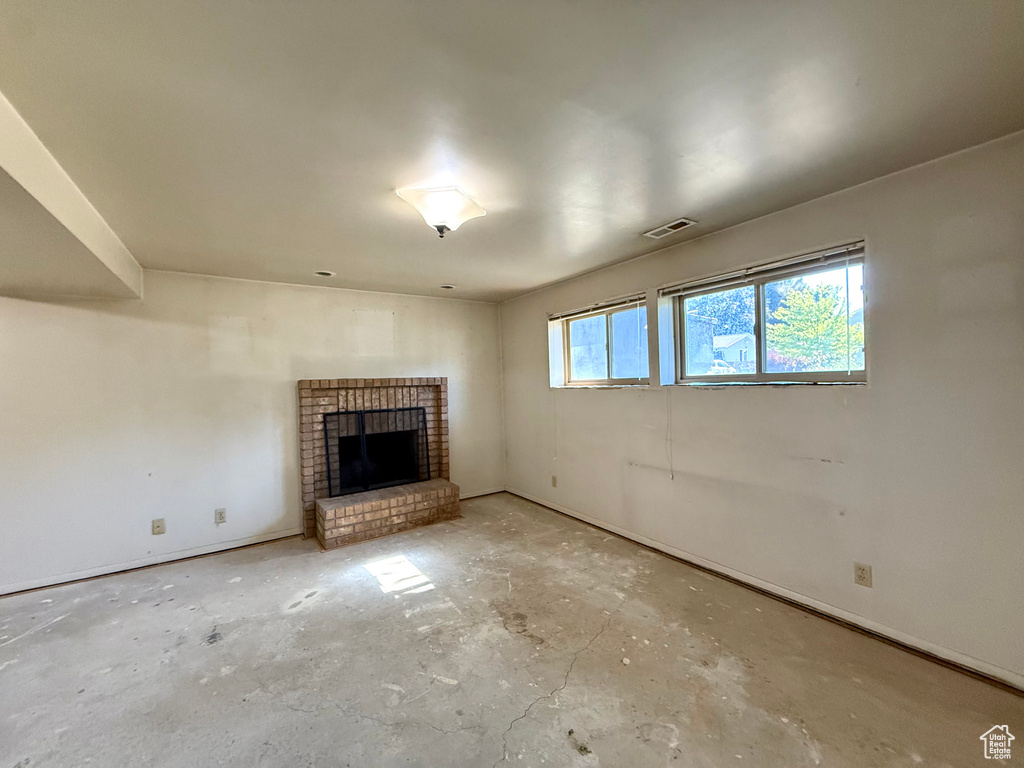 Unfurnished living room with unfinished concrete floors, a brick fireplace, and baseboards
